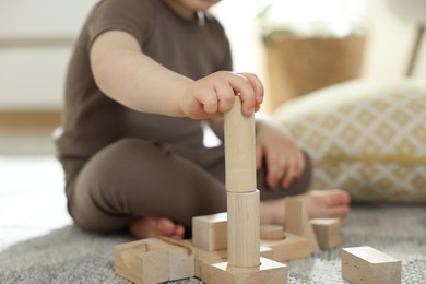 Photo of Cute little child playing with wooden building blocks at home, closeup