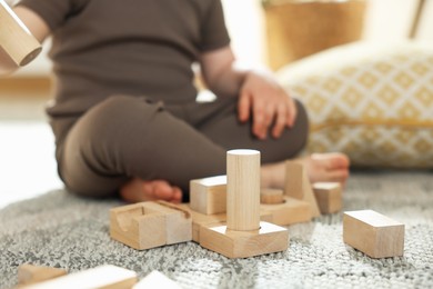 Photo of Cute little child playing with wooden building blocks at home, closeup