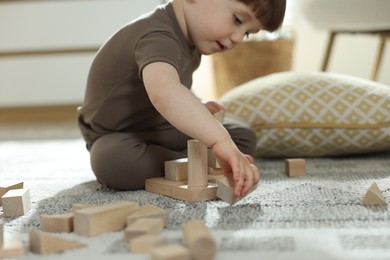 Photo of Cute little child playing with wooden building blocks at home, closeup