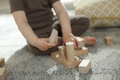 Photo of Cute little child playing with wooden building blocks at home, closeup