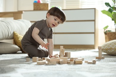 Photo of Cute little child playing with wooden building blocks at home. Space for text