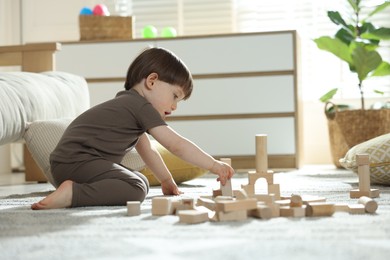 Photo of Cute little child playing with wooden building blocks at home