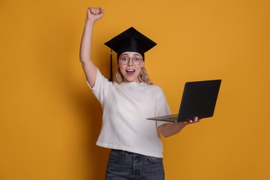 Photo of Happy student with laptop after graduation on orange background
