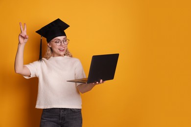 Photo of Happy student with laptop showing peace sign after graduation on orange background. Space for text