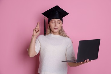 Photo of Emotional student with laptop crossing fingers on pink background. Hope for good graduation