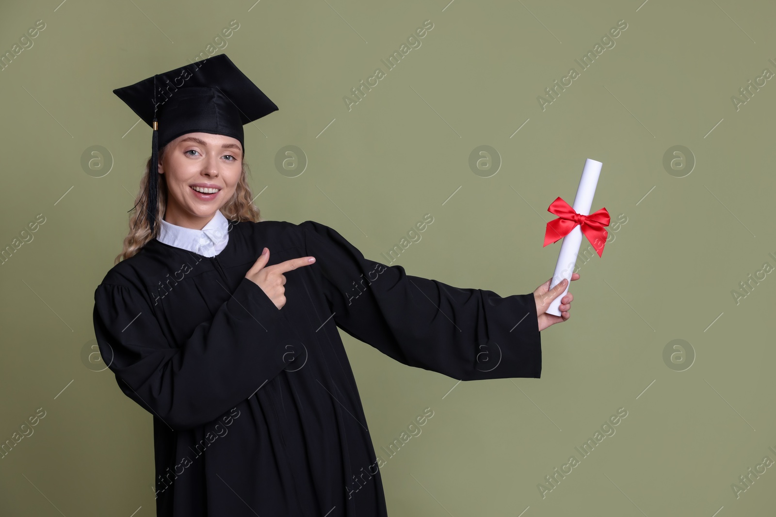 Happy student pointing at diploma after graduation on green background Photo of Happy student pointing at diploma after graduation on green background