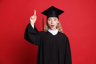 Photo of Excited student pointing upwards after graduation on red background