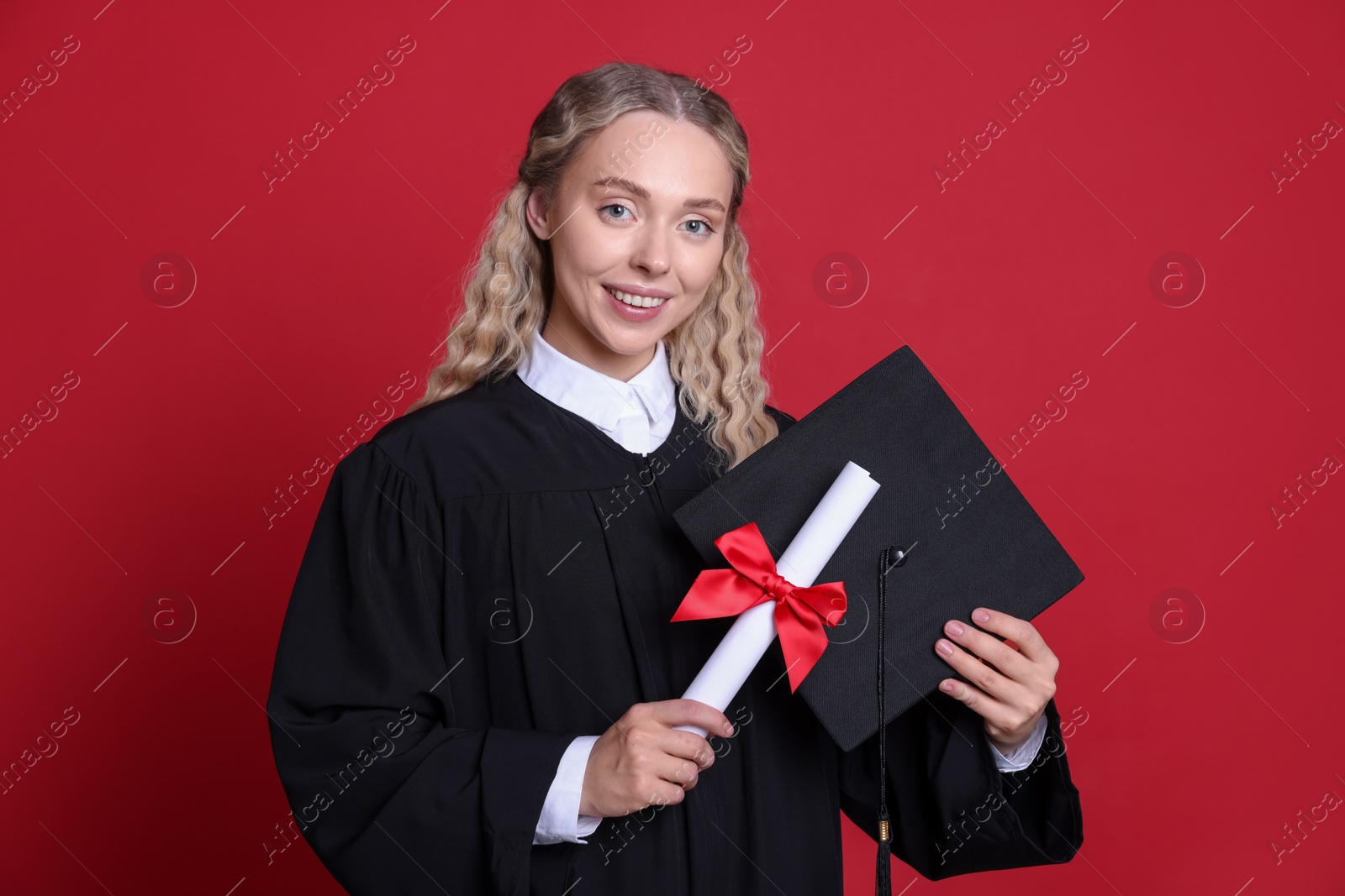 Photo of Happy student with diploma and mortarboard after graduation on red background