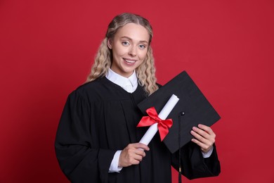 Photo of Happy student with diploma and mortarboard after graduation on red background