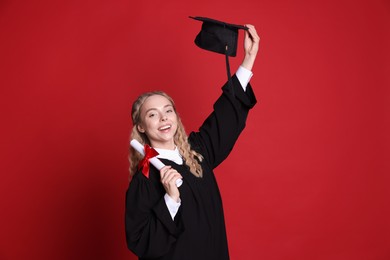 Photo of Happy student with diploma and mortarboard after graduation on red background