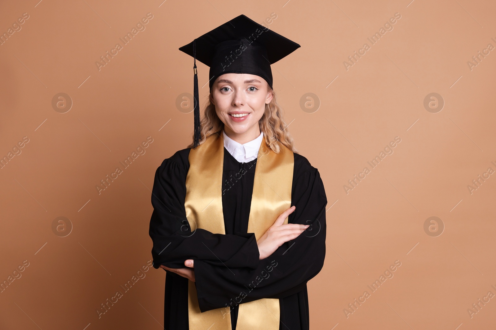 Happy student with crossed arms after graduation on beige background Photo of Happy student with crossed arms after graduation on beige background