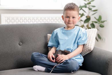 Photo of Little boy with his pet rat on sofa at home. Space for text