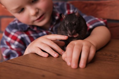 Photo of Little boy with his pet rat at wooden table indoors, closeup