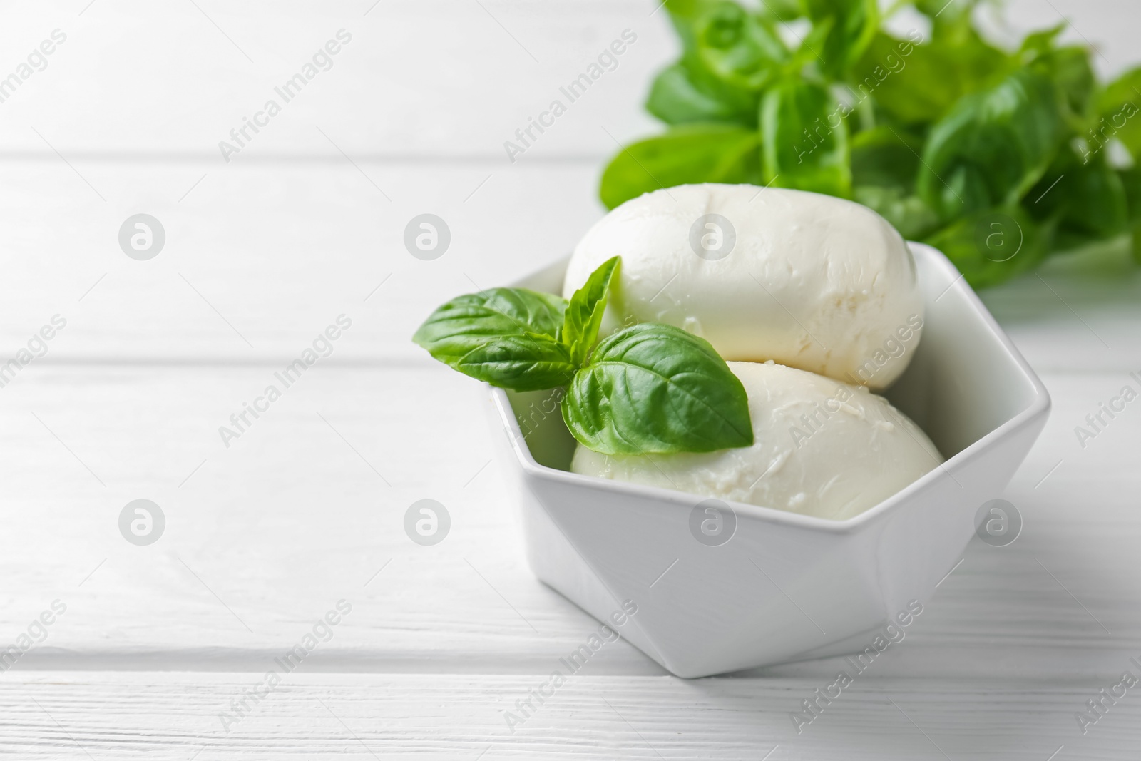 Pieces of delicious mozzarella cheese and basil in bowl on white wooden table, closeup. Space for text Photo of Pieces of delicious mozzarella cheese and basil in bowl on white wooden table, closeup. Space for text
