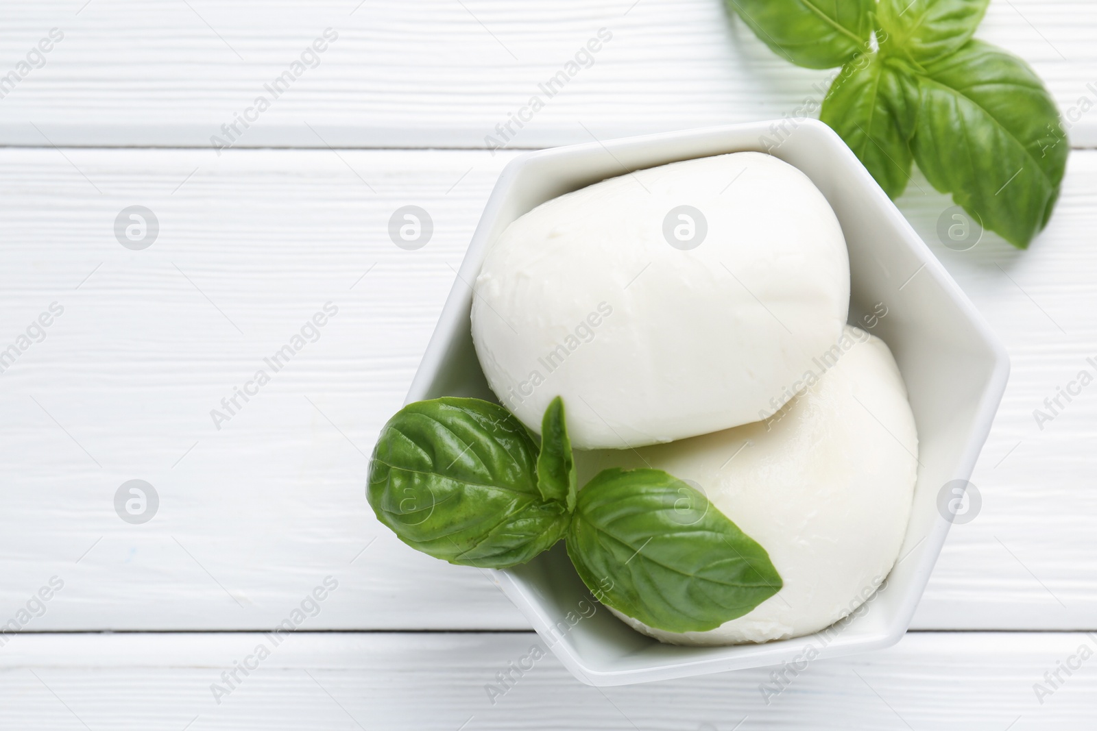 Pieces of delicious mozzarella cheese and basil in bowl on white wooden table, flat lay. Space for text Photo of Pieces of delicious mozzarella cheese and basil in bowl on white wooden table, flat lay. Space for text