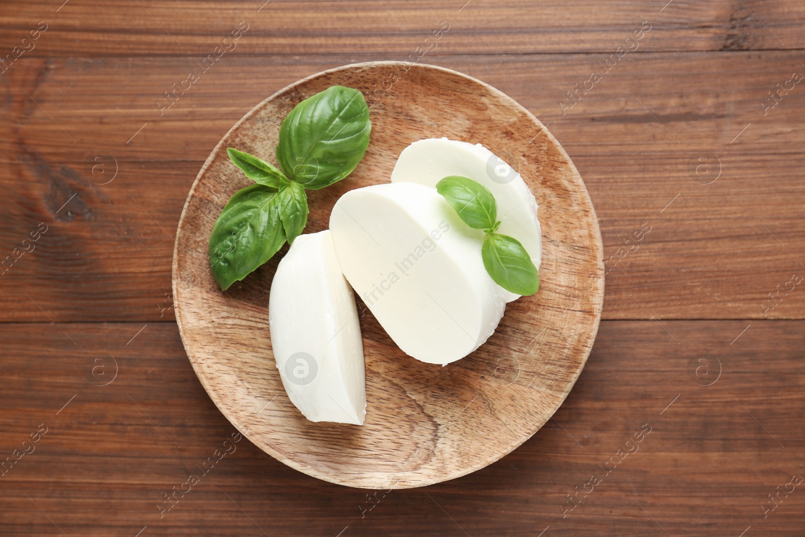 Pieces of delicious mozzarella cheese and basil leaves on wooden table, top view Photo of Pieces of delicious mozzarella cheese and basil leaves on wooden table, top view