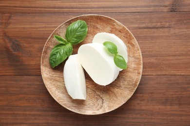 Photo of Pieces of delicious mozzarella cheese and basil leaves on wooden table, top view