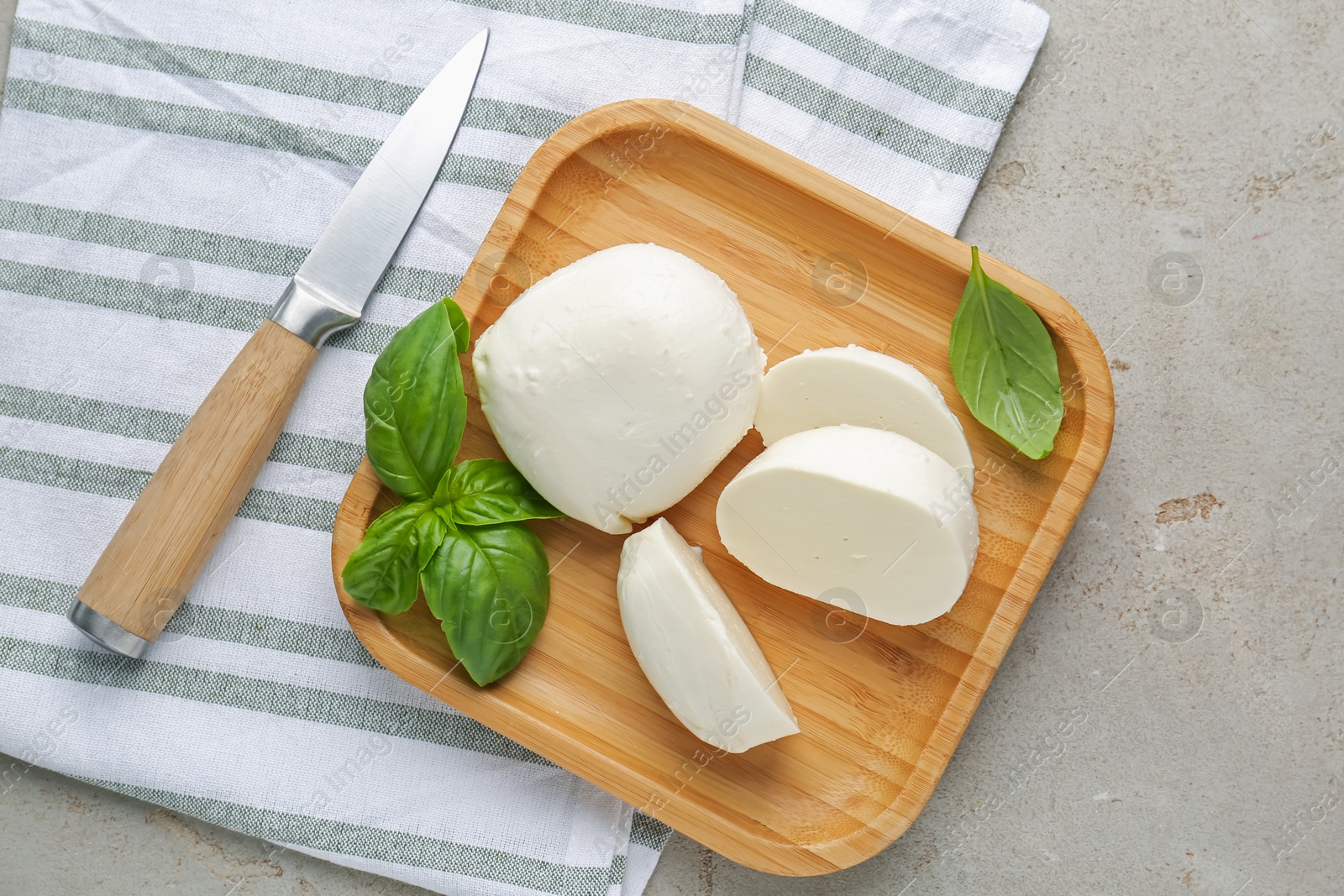 Pieces of delicious mozzarella cheese, basil leaves and knife on grey textured table, flat lay Photo of Pieces of delicious mozzarella cheese, basil leaves and knife on grey textured table, flat lay