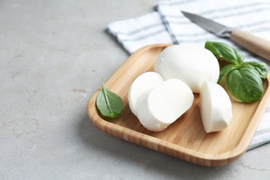 Photo of Pieces of delicious mozzarella cheese and basil leaves on grey textured table, closeup. Space for text
