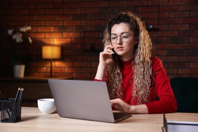 Photo of Woman talking by smartphone at desk with laptop in home office