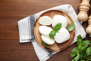Photo of Pieces of delicious mozzarella cheese, basil leaves and shakers on wooden table, flat lay