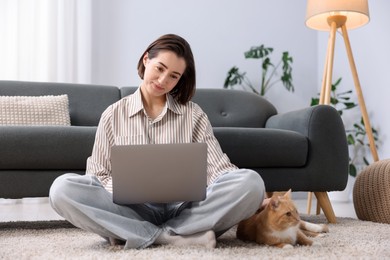Photo of Woman working with laptop and cat on floor in home office