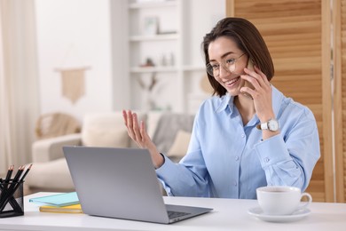 Photo of Smiling woman talking by smartphone with laptop at desk in home office