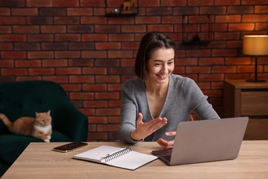Photo of Smiling woman having videochat by laptop at desk in home office