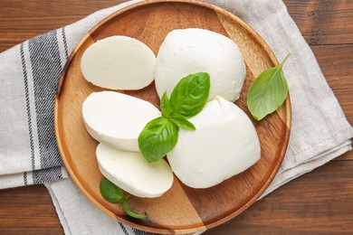 Photo of Pieces of delicious mozzarella cheese and basil leaves on wooden table, top view