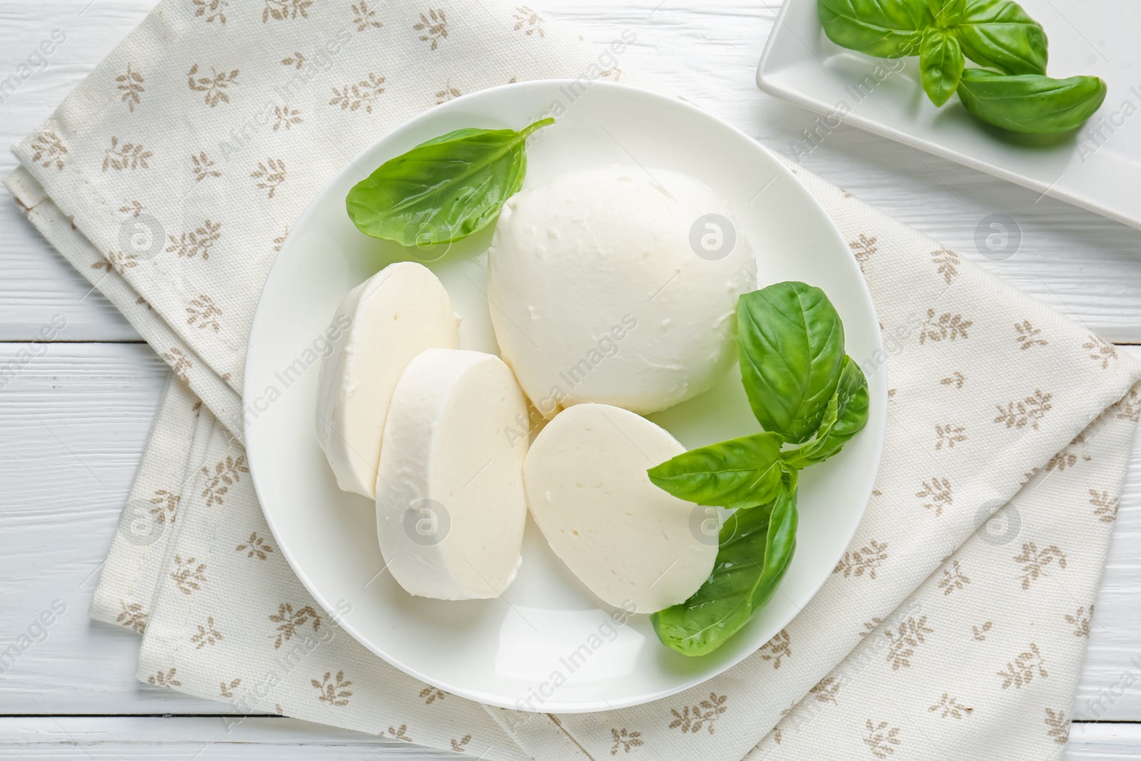 Pieces of delicious mozzarella cheese and basil on white wooden table, flat lay Photo of Pieces of delicious mozzarella cheese and basil on white wooden table, flat lay