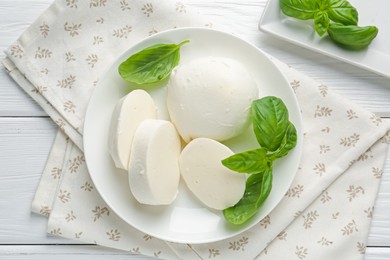 Photo of Pieces of delicious mozzarella cheese and basil on white wooden table, flat lay