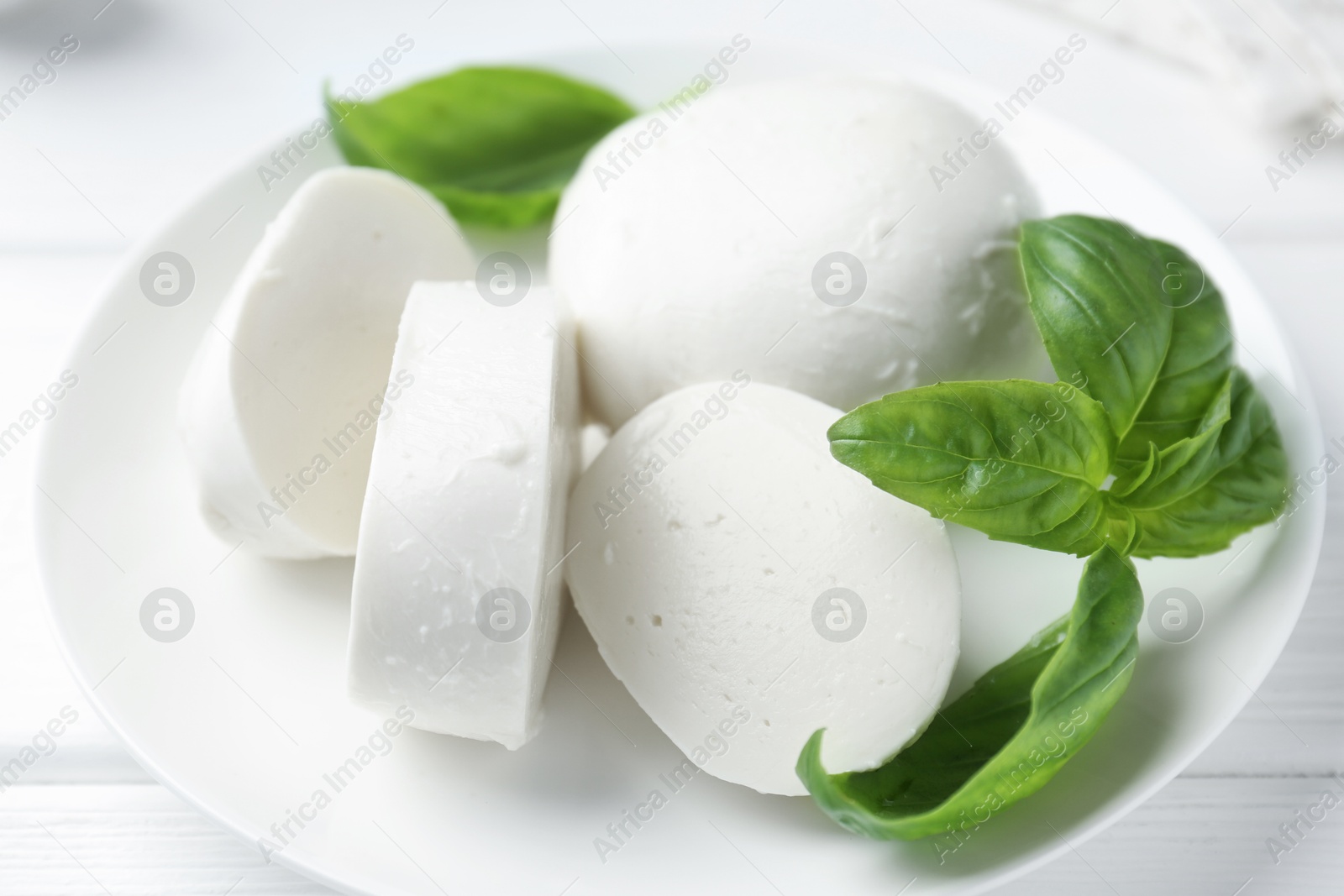 Pieces of delicious mozzarella cheese and basil on white wooden table, closeup Photo of Pieces of delicious mozzarella cheese and basil on white wooden table, closeup