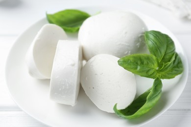 Photo of Pieces of delicious mozzarella cheese and basil on white wooden table, closeup