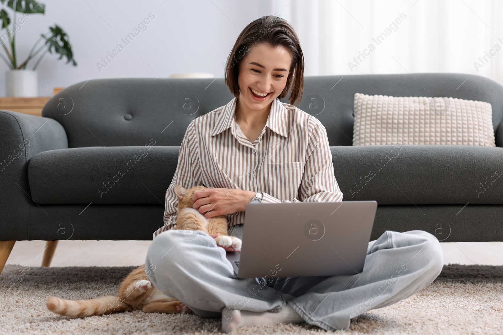 Smiling woman working with laptop and cat on floor in home office Photo of Smiling woman working with laptop and cat on floor in home office