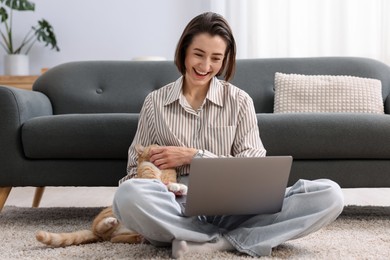 Photo of Smiling woman working with laptop and cat on floor in home office
