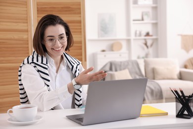 Photo of Smiling woman having videochat by laptop at desk in home office