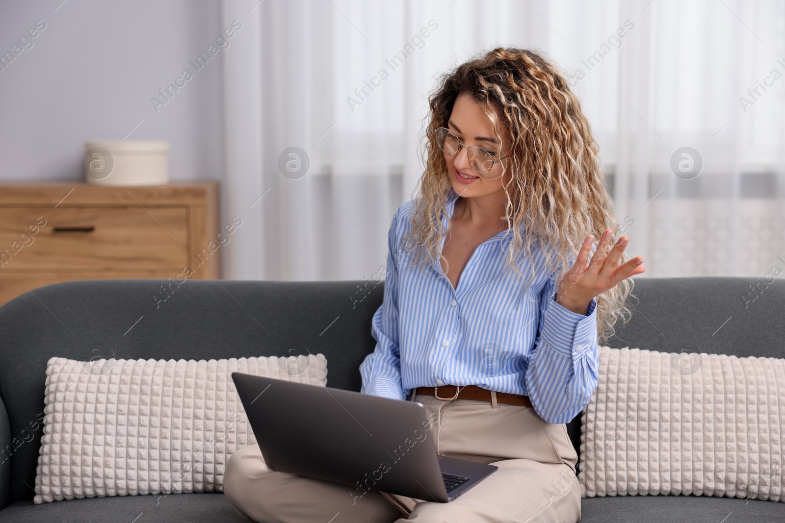 Photo of Smiling woman having videochat by laptop on sofa in home office
