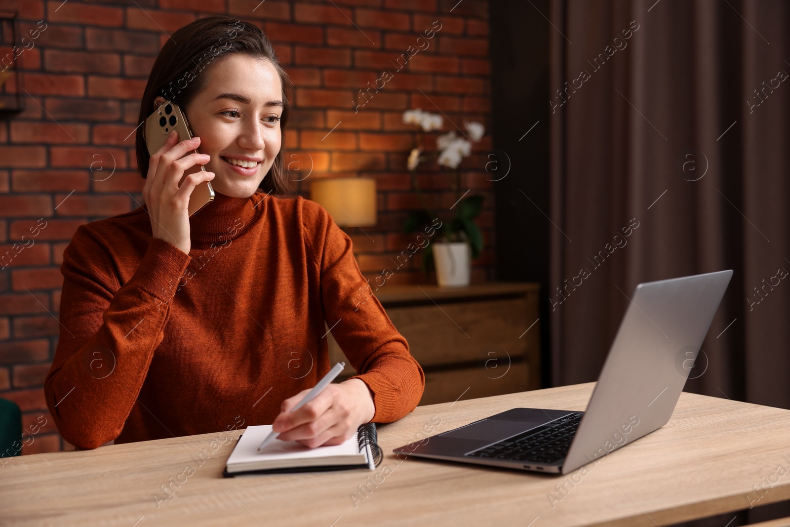 Smiling woman talking by smartphone and working at desk in home office Photo of Smiling woman talking by smartphone and working at desk in home office