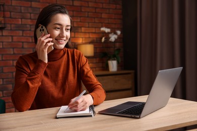 Photo of Smiling woman talking by smartphone and working at desk in home office