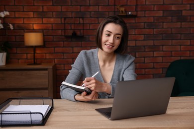 Photo of Smiling woman having videochat by laptop at desk in home office