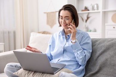 Photo of Smiling woman talking by smartphone with laptop on sofa in home office