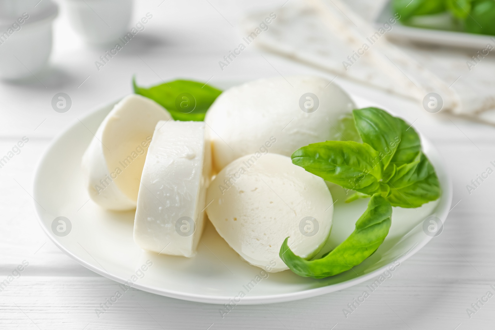 Pieces of delicious mozzarella cheese and basil on white wooden table, closeup Photo of Pieces of delicious mozzarella cheese and basil on white wooden table, closeup