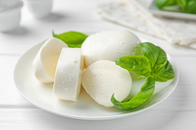 Photo of Pieces of delicious mozzarella cheese and basil on white wooden table, closeup