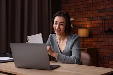 Photo of Woman having videochat by laptop at desk in home office