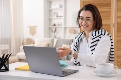 Photo of Smiling woman having videochat by laptop at desk in home office