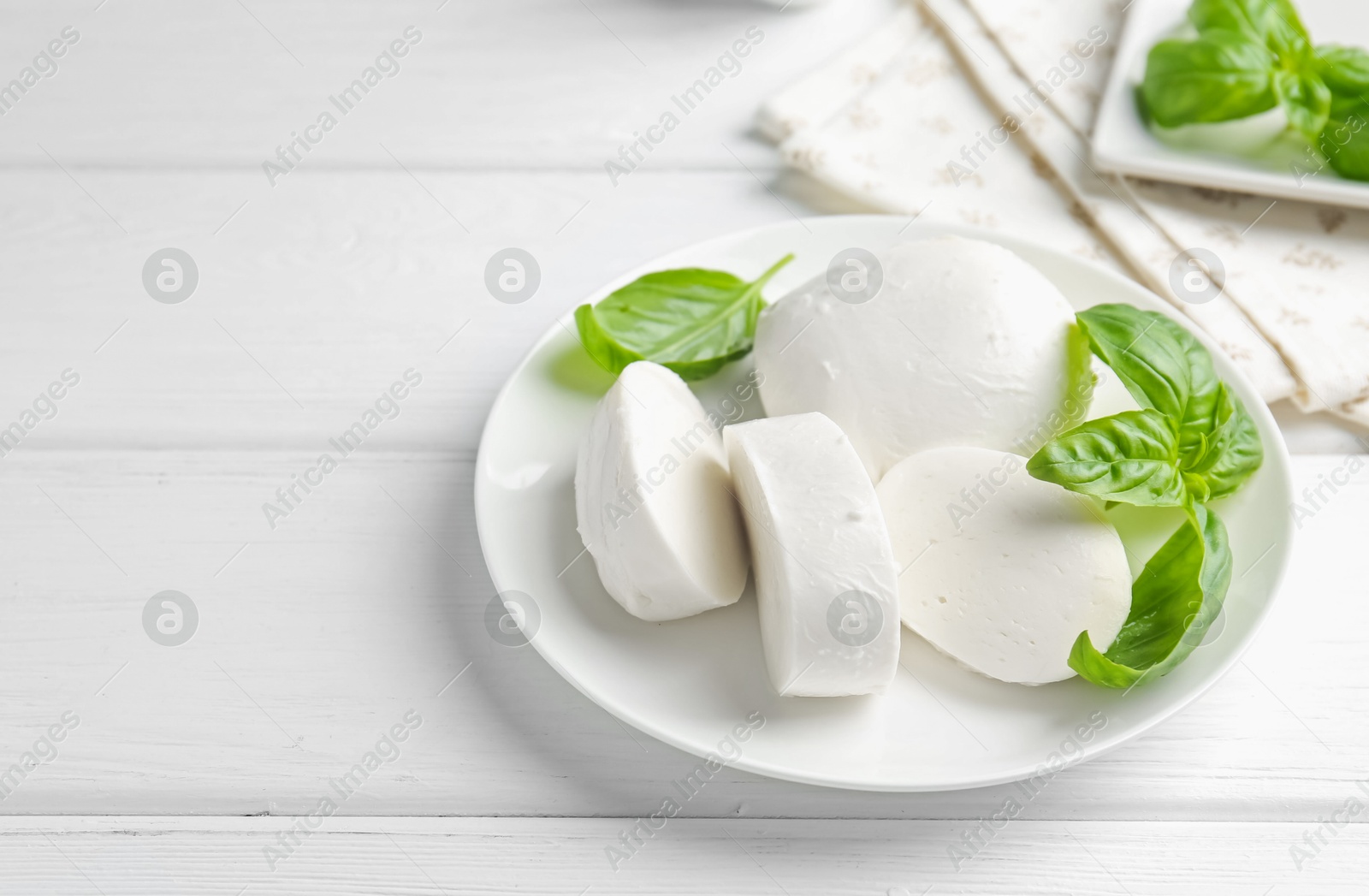 Pieces of delicious mozzarella cheese and basil on white wooden table. Space for text Photo of Pieces of delicious mozzarella cheese and basil on white wooden table. Space for text