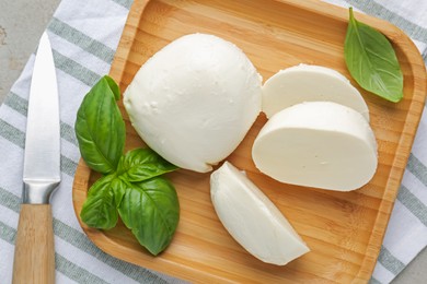 Photo of Pieces of delicious mozzarella cheese, basil leaves and knife on grey table, top view