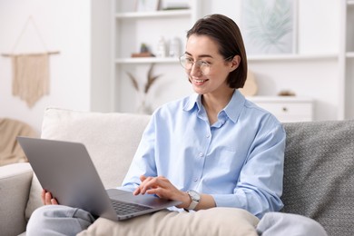 Photo of Smiling woman working with laptop on sofa in home office