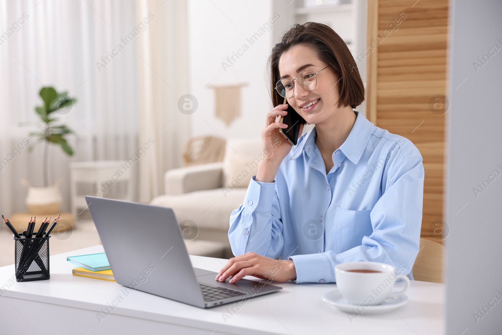 Smiling woman talking by smartphone with laptop at desk in home office Photo of Smiling woman talking by smartphone with laptop at desk in home office
