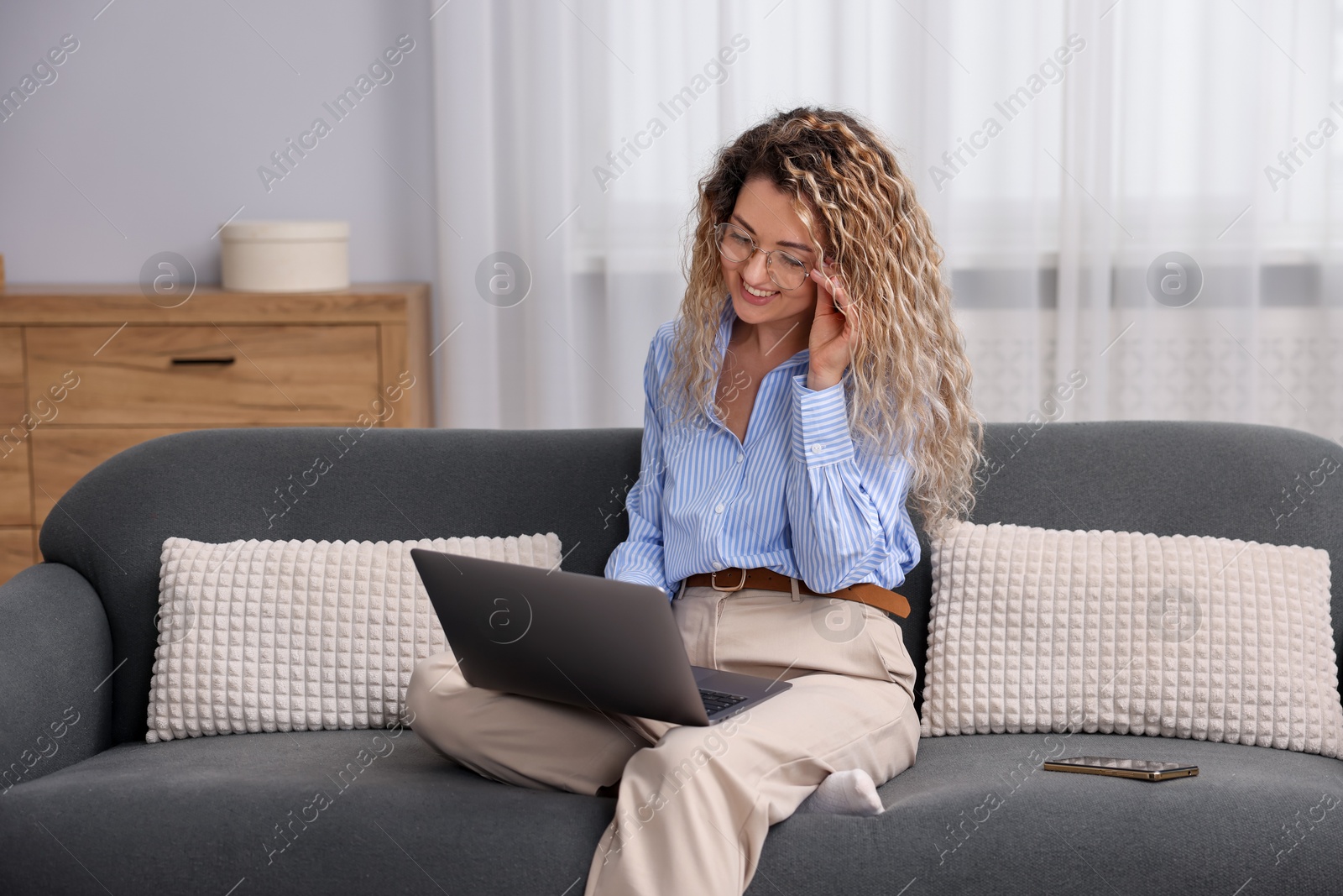 Smiling woman having videochat by laptop on sofa in home office Photo of Smiling woman having videochat by laptop on sofa in home office